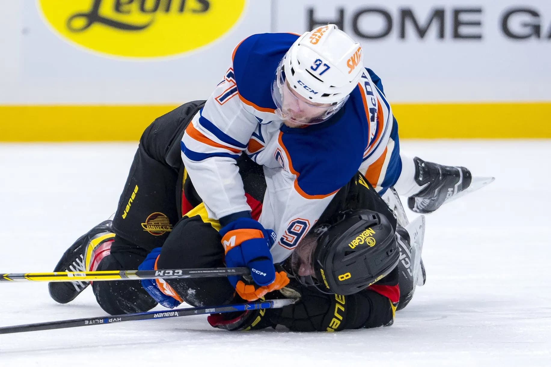 Eishockey Spieler Connor McDavid in einem weissen liegt auf Eishockeyspieler Conor Garland in einem schwarzen Trikot. Die Spieler liegen auf der Eisfläche und rangeln.